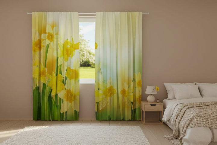Natural sunlight streams into the bright and modern living room interior. A large bed is visible on the right. Photo curtains are hung on the window, featuring photorealistic images of large, yellow daffodils with green stems against a soft yellow and light green sunlit background.