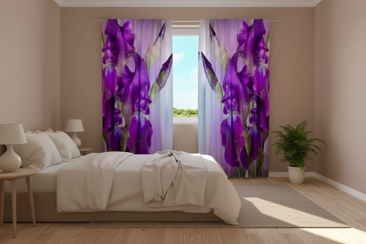 A bright, modern bedroom interior bathed in natural sunlight. To the left is a large, light-colored bed. Photo curtains are hung on the window, featuring large, vivid purple iris flowers and green buds depicted in extreme close-up (macro) with photorealistic detail. Fine dewdrops are visible on the petals. In the middle of the open curtains is a window with a view of green trees and a blue sky.