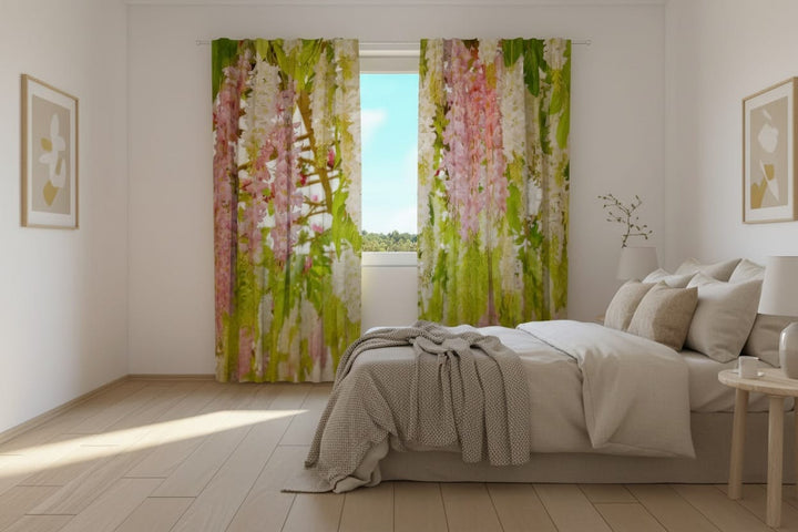 A bright bedroom interior with wooden floors and a large bed in light tones. Photo curtains are hung on the window, featuring a photorealistic depiction of a spring garden motif—abundant, drooping clusters of soft pink and white flowers (similar to wisteria) and fresh green foliage.