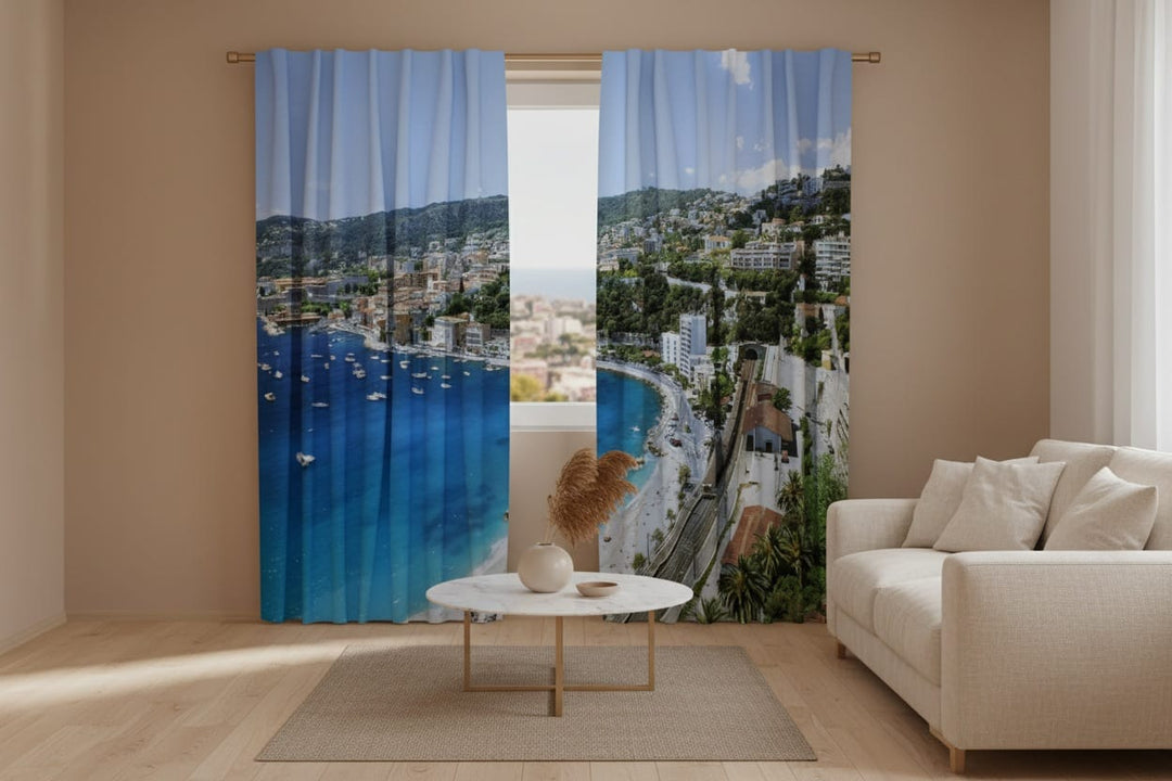 Bright living room interior with wooden floors and light-colored furniture. Photo curtains are hung on the window, featuring a photorealistic depiction of a picturesque Mediterranean (Greek) coastal town from a high vantage point.