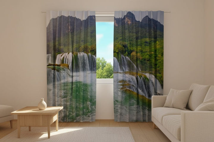 Living room interior with light-colored furniture and a photo curtain. Photo curtains are installed on the window, featuring a photorealistic depiction of a large, multi-tiered waterfall.