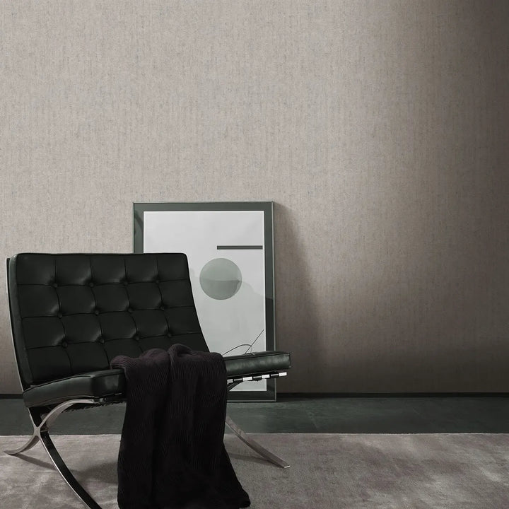 Light gray textured wallpaper in a modern interior with a black leather armchair, a throw blanket, and abstract artwork