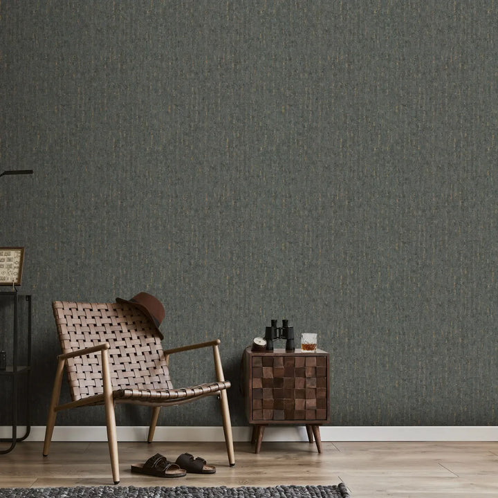 Dark gray textured wallpaper with gold accents in a modern interior with a woven leather armchair and a wooden table
