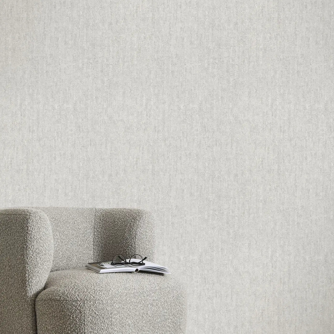 Light gray textured wallpaper in a minimalist interior with a soft armchair, an open book, and reading glasses