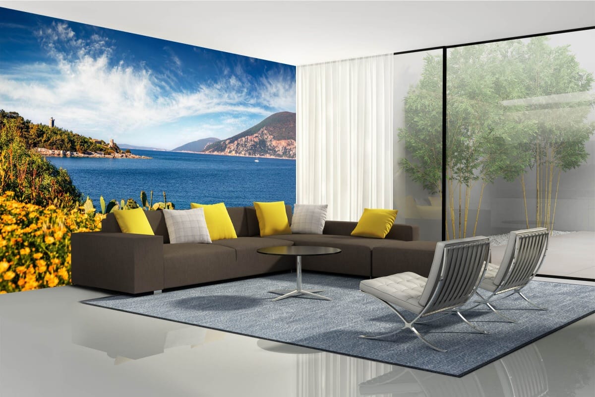 A spacious living room with a brown sofa and realistic photo wallpaper depicting a beautiful ocean view: a blue sea, a green coastline, and a cloudless sky.