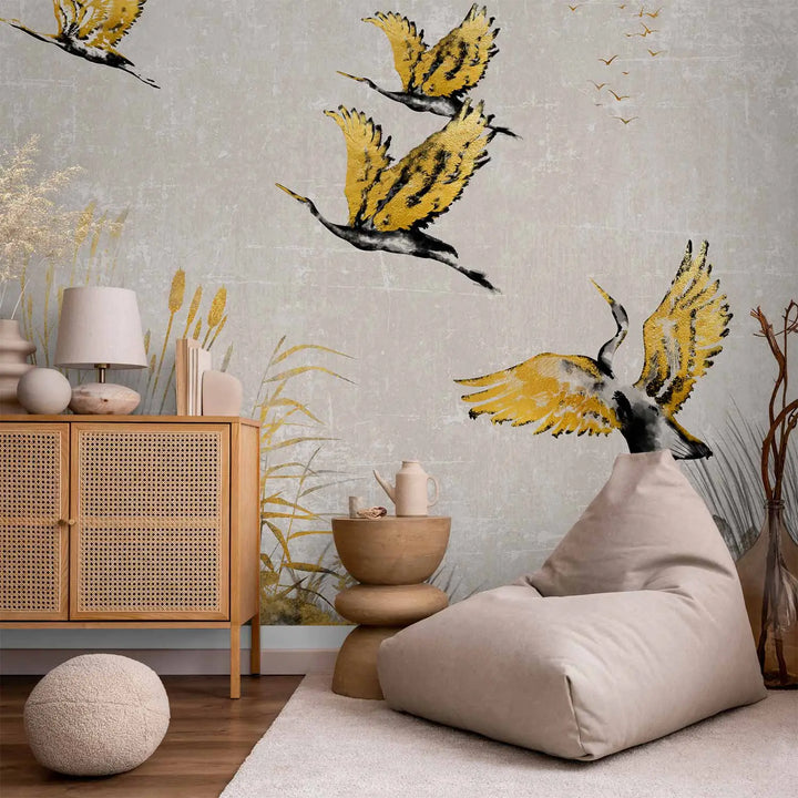 Photo wallpaper with a golden cranes and reeds motif in a lounge area interior behind a soft beanbag, a wooden chest of drawers with wicker door inserts, and a rug