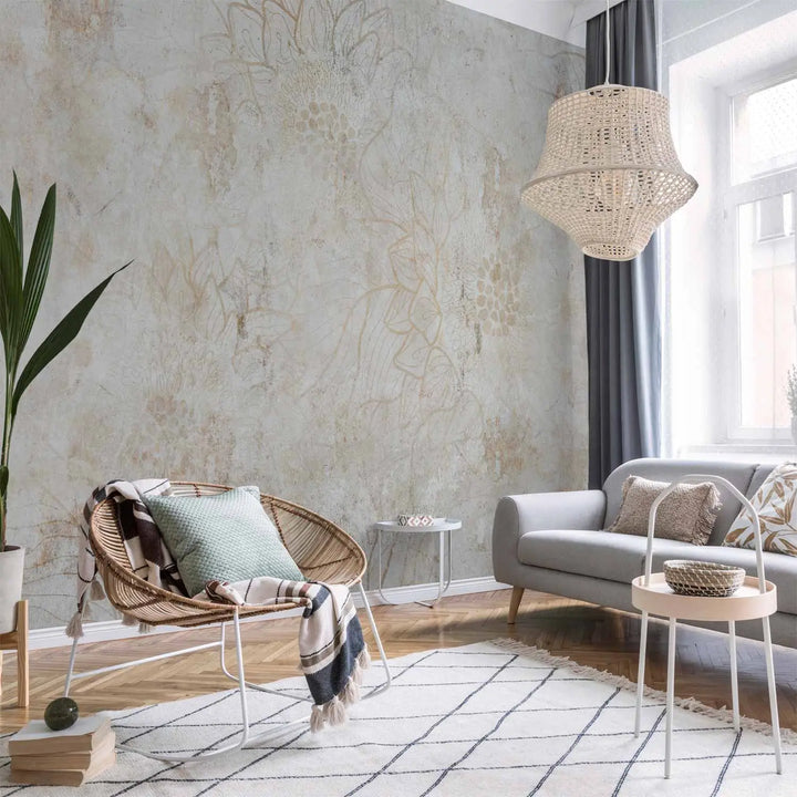 Photo wallpaper with a vintage floral motif in a living room interior with a wicker rocking chair, a grey sofa, and a natural wood parquet floor with a rug
