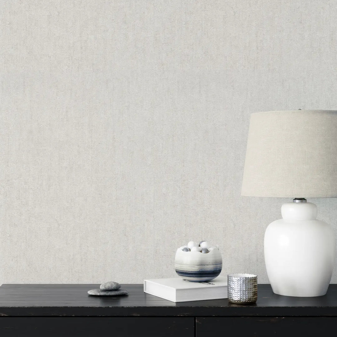 Light gray textured wallpaper in an interior with a dark wood console table, white table lamp, and minimalist decorative elements