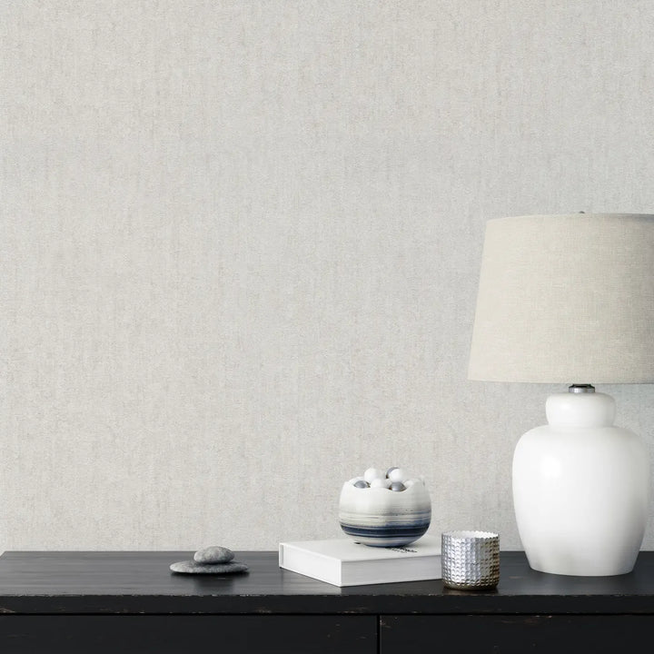 Light gray textured wallpaper in an interior with a dark wood console table, white table lamp, and minimalist decorative elements