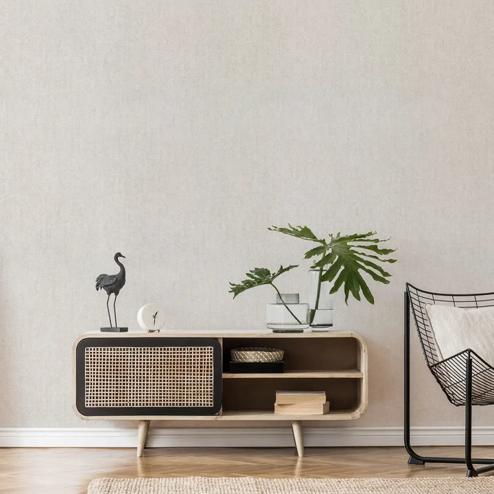 Light gray textured wallpaper in a modern interior with a wooden dresser, black decorative bird, and green tropical plants in glass vases