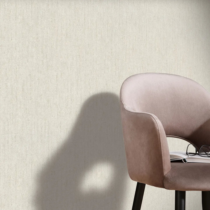 Light beige textured wallpaper in a modern interior with an elegant velvet armchair, an open book, and reading glasses